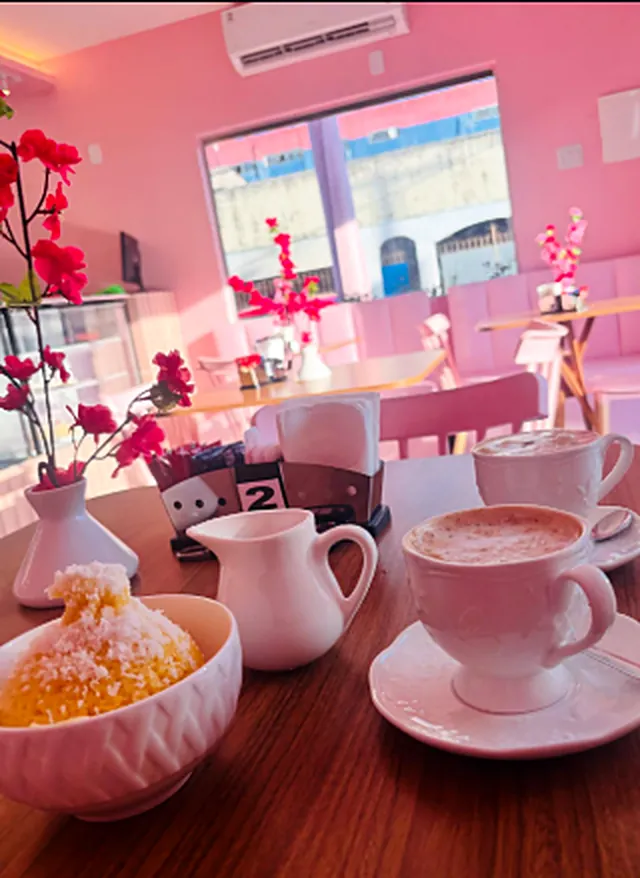 Mesa com dois cappuccinos, jarrinha de leite e um doce com coco ralado