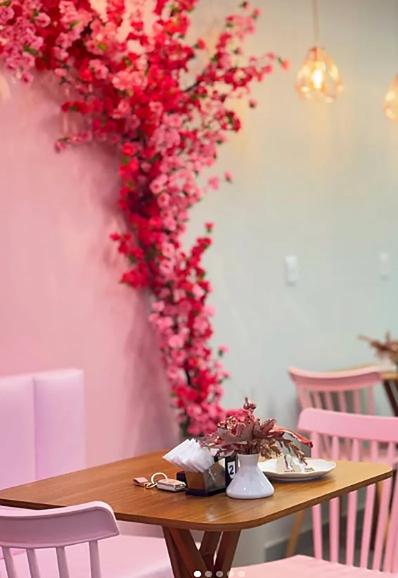 Parede rosa com galhos de flores de cerejeira e uma mesa de madeira com flores