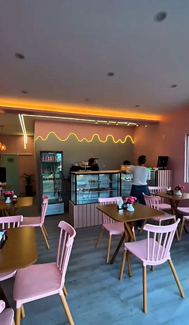 Salão com cadeiras rosa, mesas de madeira e uma linha de neon âmbar ondulada na parede do balcão